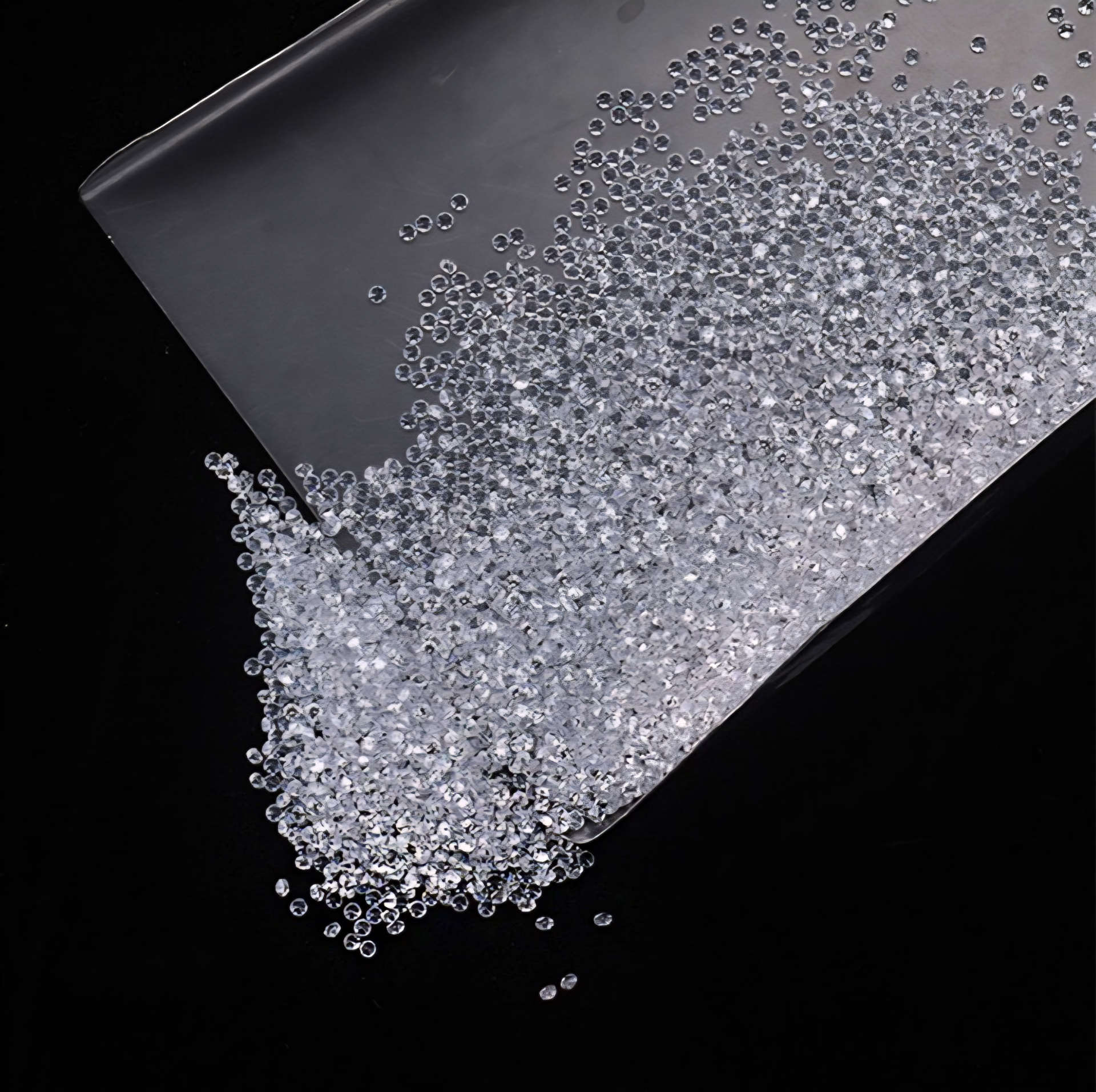 Loose lab-grown melee diamonds pouring from a folded parcel paper on black